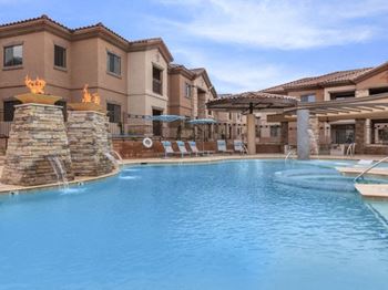 A large swimming pool with a fountain and a resort style building in the background
